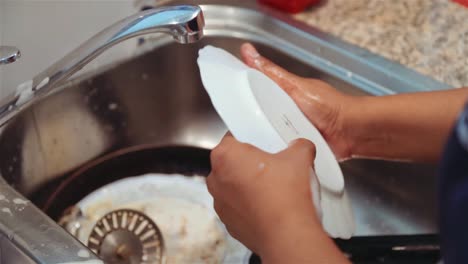 washing and scrubbing dirty plates over a sink. handheld shot. close up.