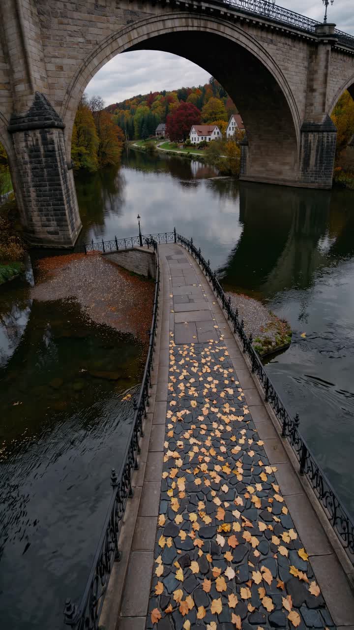A serene video scene capturing a bridge over a calm river, viewed from a high angle, with autumn