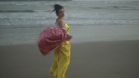 A-woman-in-a-red-cardigan-and-golden-outfit-walks-away-from-the-camera-on-a-windy-beach