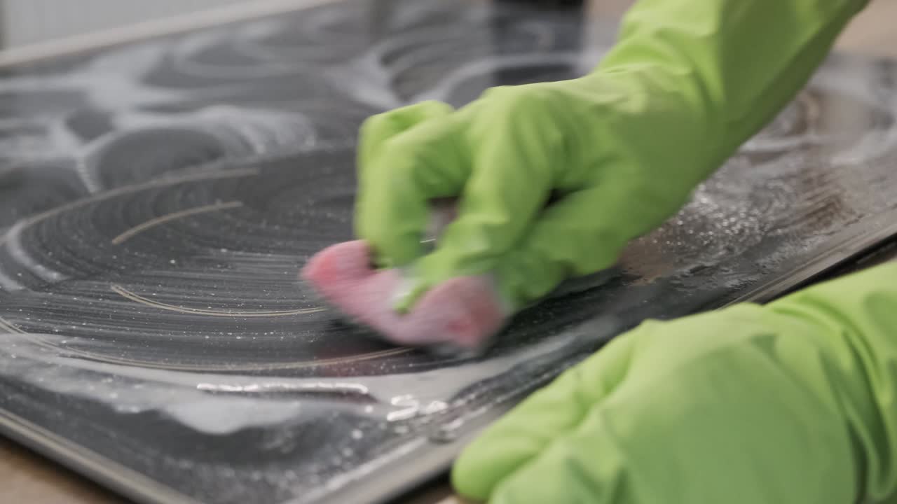 손 여성이 스폰지와 세제로 현대 요리 유리 세라 전기 표면을 청소하는 클로즈업