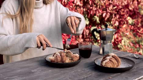 Parisian-woman-having-a-french-breakfast-while-cutting-a-croissant-and-drinking-coffee,-faceless-person