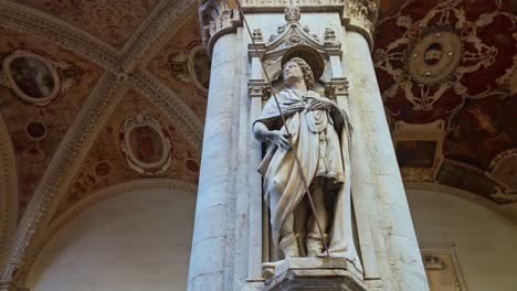 una estatua adorna un pilar de la logia de los comerciantes, loggia della mercanzia ubicada detrás de la plaza del campo, en siena, italia