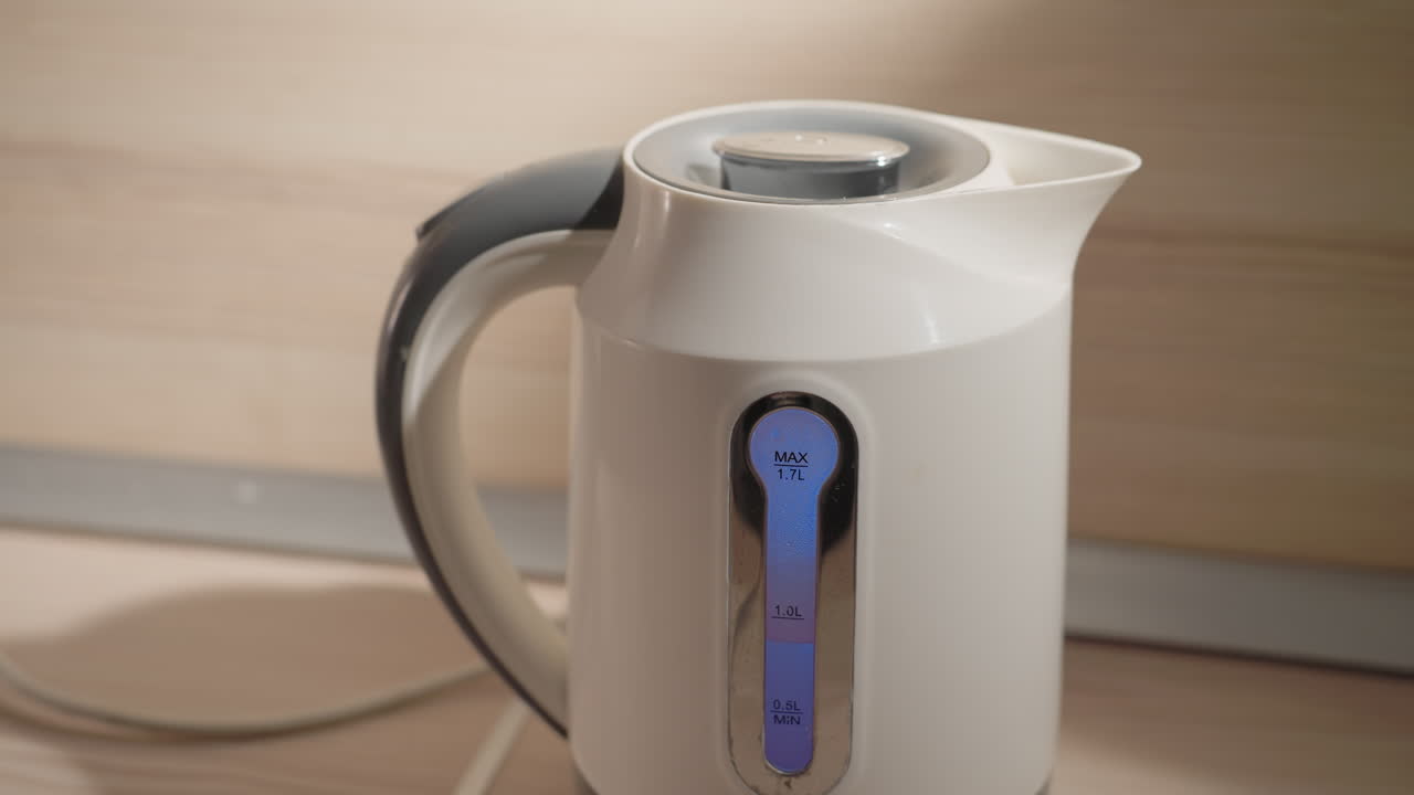 Close-up of electric kettle with visible water level indicator in minimalist kitchen. Soft light highlights clean design, modern appliance, and sleek lines on countertop in serene setting