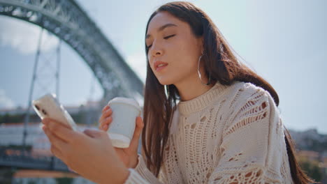relaxed woman surfing phone at sunny river bank closeup. girl sipping coffee