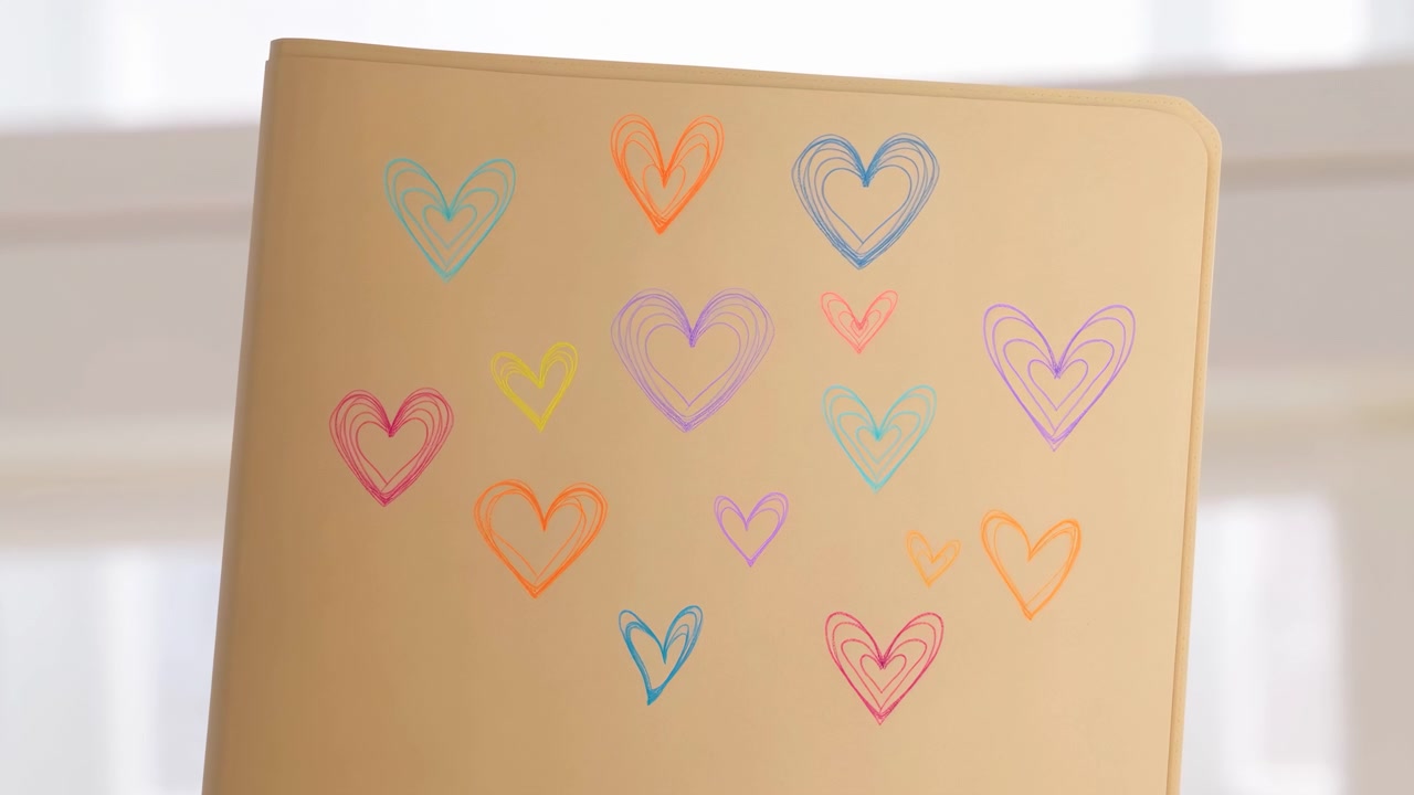 Primer plano de un cuaderno o tarjeta beige decorado con pequeños corazones pastel dibujados a mano, colocado ligeramente a la izquierda del centro sobre un fondo interior luminoso y suavemente desenfocado