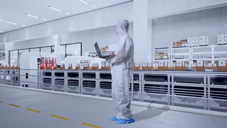 full body side view of asian male scientist typing on a laptop and looking around with conveyor for packaging coffee beans in bags at coffee factory