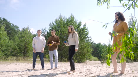 caucasian young woman throwing a petanque ball on the beach on a sunny day while her friends wait their turns