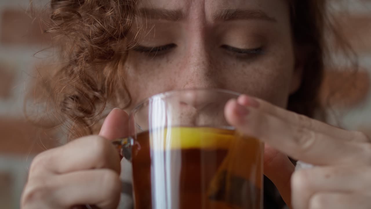 vídeo en primer plano de una mujer caucásica pelirroja tomando té frío y caliente en la sala de estar.