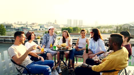 multiracial group of friends is having open air party drinking, talking and laughing enjoying summer and good company. youth, city and celebration concept.