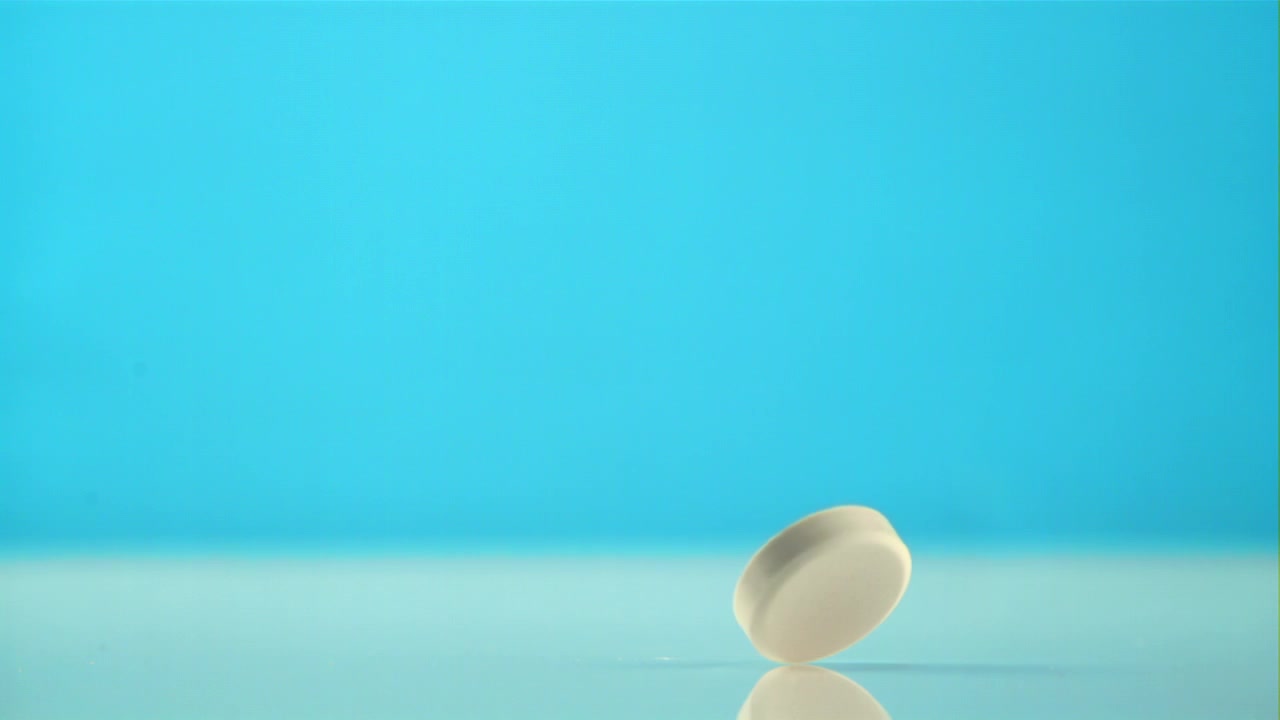 White Pill Falling and Bouncing in Slow Motion on Blue Background