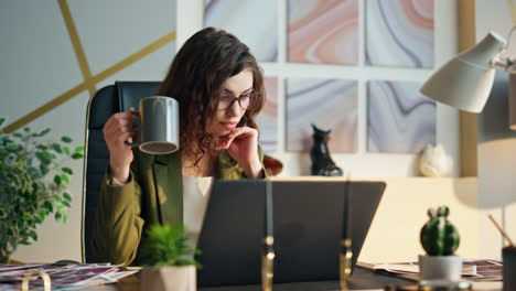 business woman holding coffee sitting office desk close up. girl looking laptop.