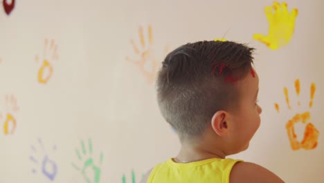madre y su lindo niño se divierten felices juntos dejando sus coloridas huellas de manos en la pared. madre toma en brazos su sol para ayudarlo a hacer su huella de mano