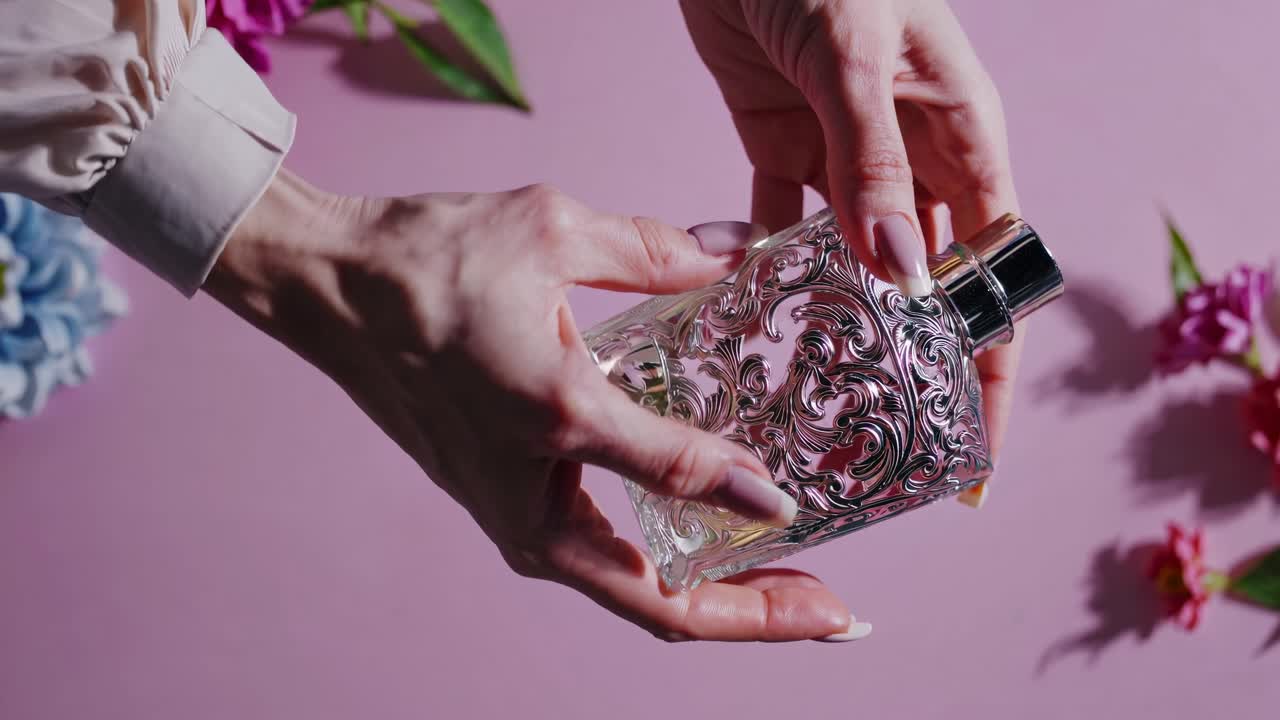 Video ravvicinato di mani che tengono un'elaborata boccetta di profumo su uno sfondo rosa.