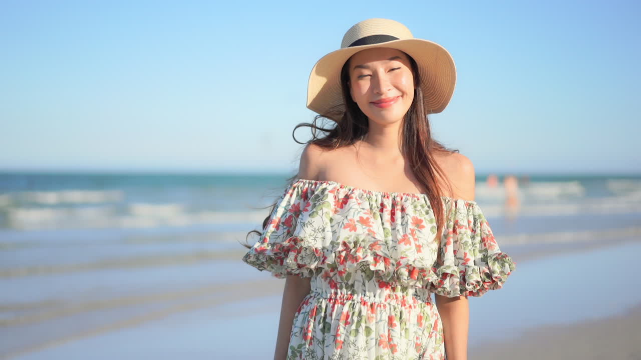 Portrait of Pretty Asian Female Standing on Beach in Summer Dress and Hat and Looking at Camera