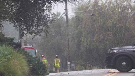 dos bomberos caminando bajo la lluvia con una patrulla bloqueando la carretera