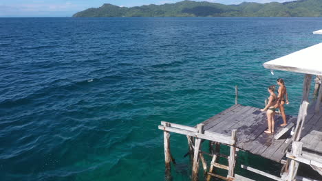 girls jumping from a pier into the turquoise sea