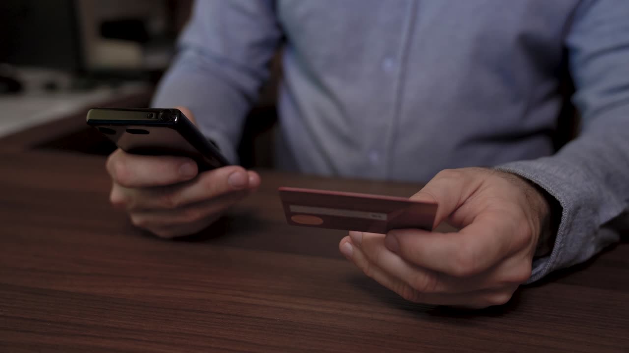 un hombre de negocios tiene un teléfono móvil en una mano y una tarjeta de crédito en la otra. usa su tarjeta de crédito para pagar en línea usando su celular.