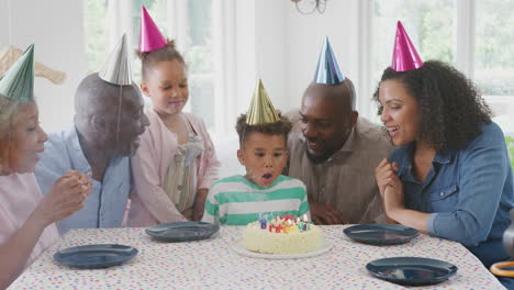 Mehrgenerationenfamilie-Sitzt-Am-Tisch-Und-Feiert-Den-Geburtstag-Des-Jungen,-Während-Er-Kerzen-Ausbläst