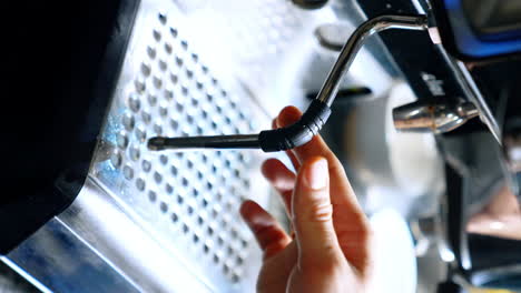 coffee making machine close up. male hands hold the pot filling it with hot milk. close up. vertical screen. blurred backdrop.