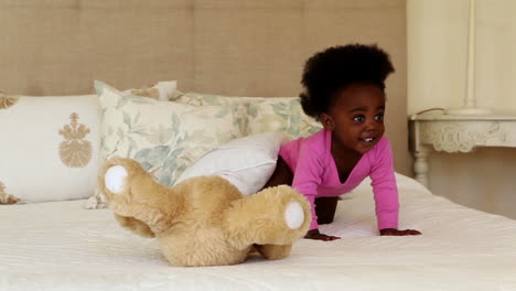 cute baby girl playing with teddy bear on bed