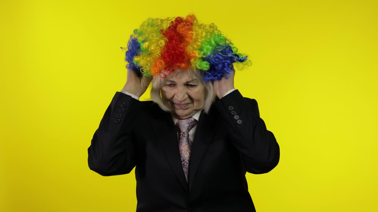 비즈니스 슈트를 입은 고위 여성이 조롱거리 가발을 입고 일하기 시작하고 미소 짓습니다.