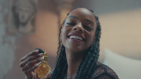chica modelo africana sentada en la cama y usando su perfume en ella durante el día