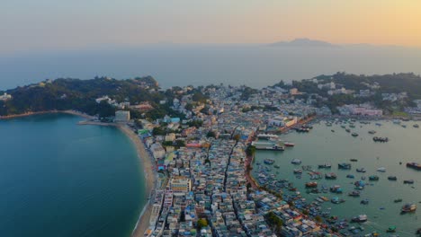 disparo de drones viajando hacia adelante sobre una ciudad construida en un istmo con un puerto y una playa popular durante la hora dorada