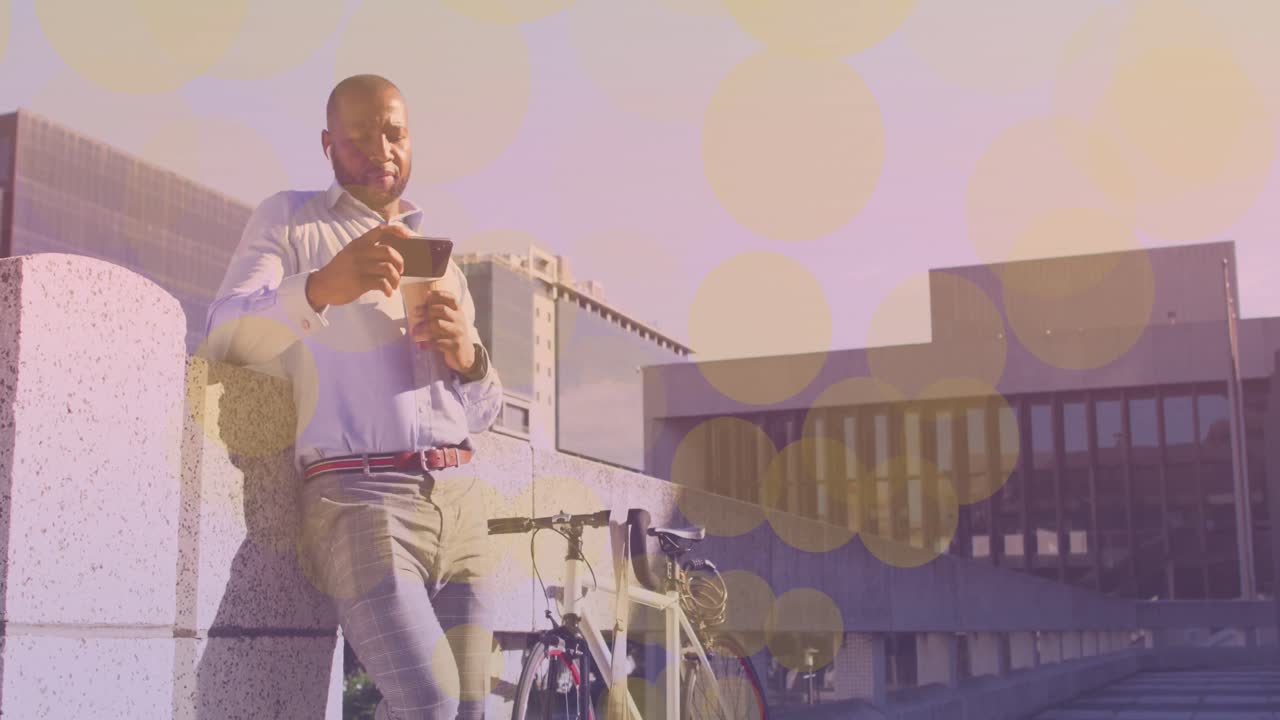Yellow spots of light floating against african american man with a bicycle using smartphone
