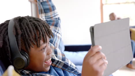 happy african american boy with headphones using tablet lying on floor at home, slow motion