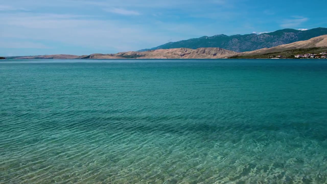 Prachtig turquoise lagunewater bij het stadsstrand van het eiland Pag met kale heuvels en het Velebitgebergte, Kroatië
