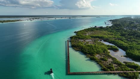 Vista-Aérea-De-Un-Barco-Que-Pasa-Por-El-Muelle-En-El-área-Natural-Protegida-Parque-Laguna-De-Bacalar,-En-El-Soleado-México