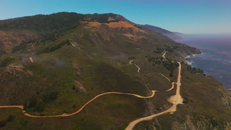 roads passing through uneven mountainous landscape of california coastline. pine tree forest overgrowing the mountain tops. aerial perspective.
