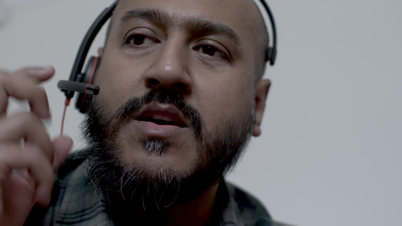 un primer plano de la cara de un representante de un centro de llamadas asiático, el hombre que intenta atender una llamada pero experimenta problemas técnicos con el audio en el micrófono de sus auriculares