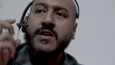 a close up shot of the face of an asian call centre representative, the man attempting to take a call but experiences technical issues with the audio on his headset microphone