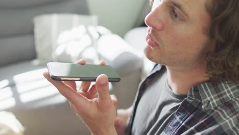 Happy-caucasian-man-sitting-on-sofa-in-living-room-talking-on-smartphone