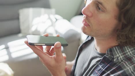 happy caucasian man sitting on sofa in living room talking on smartphone