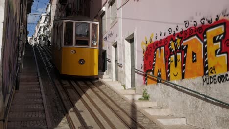 crowded carriage of the bica funicular climbing tracks of famous rua da bica in lisbon pombaline area, portugal. commuter and tourist on ride. graffitti on building walls.