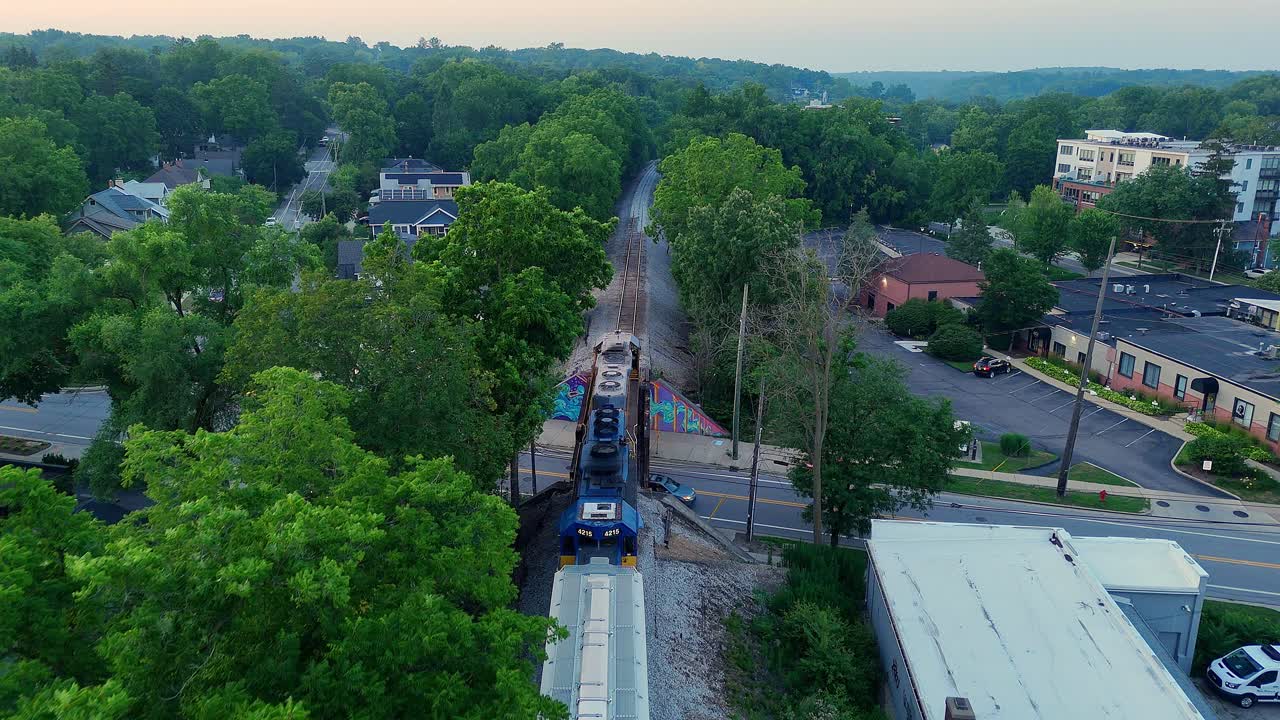Freight train runs through suburban neighborhood in Ann Arbor, Michigan, USA, aerial follow shot