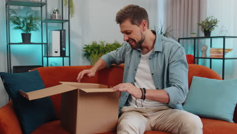 happy young man shopper unpacking cardboard box delivery parcel online shopping purchase at home