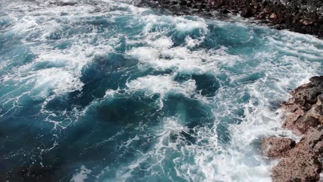 forward flight over waves into rocky beach of volcanic stone on hawaii island