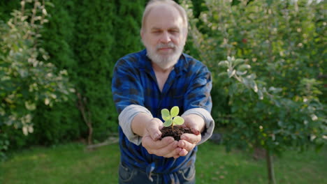 An-elderly-man-holds-a-small-plant-in-his-hands-in-the-green-garden