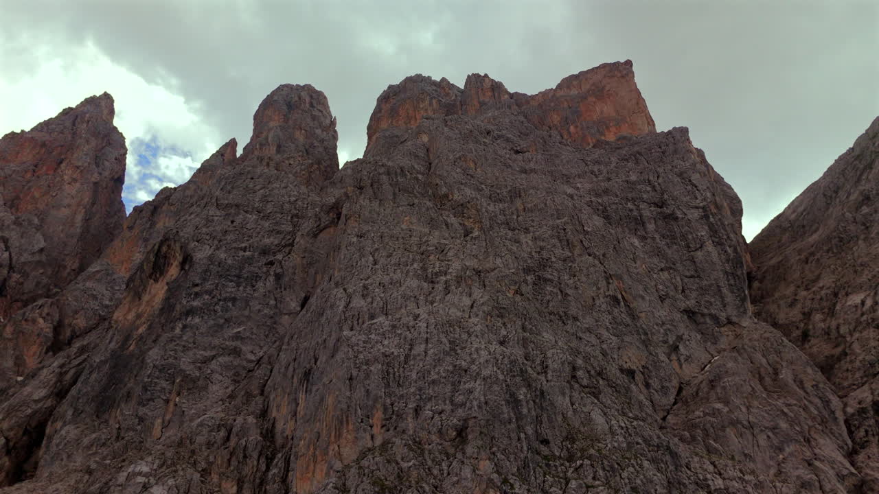 un primer plano aéreo detallado de los escarpados y altísimos acantilados rocosos en los dolomitas, italia, frente a un espectacular cielo nublado