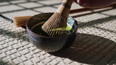aerial view of a traditional matcha bowl with a whisk, casting shadows on a woven mat