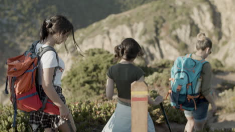 mother and daughters with trekking poles walking down hiking trail, descending steep hill