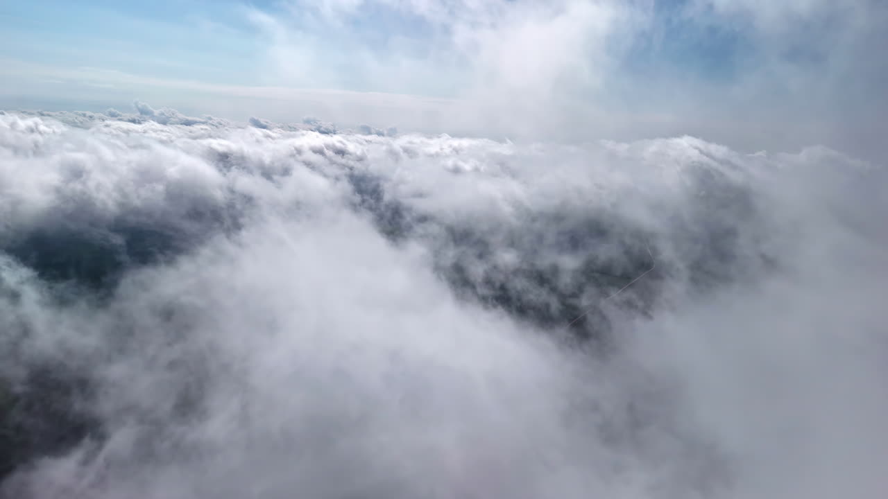 High altitude aerial view flying forward through endless white cumulus clouds with blue sky visible above