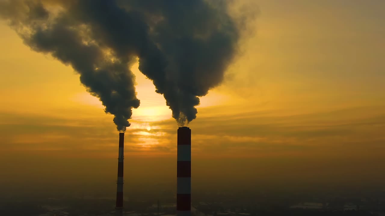 Air pollution. clouds of smoke coming from the chimneys of the plant with beautiful golden yellow lighting of setting sun. Drone flying over smoking smokestacks of a steel factory.