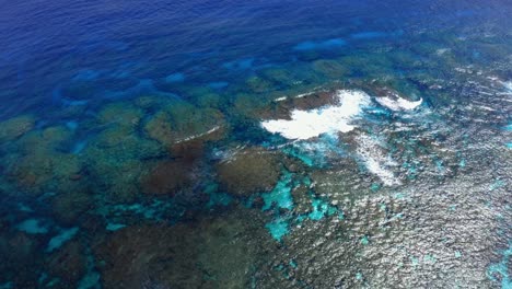 a drone view provided by the drone shows the idyllic blue lagoon, its transparency revealing the hidden beauty of the rocks and sea-life, while the waves crashing on the reef