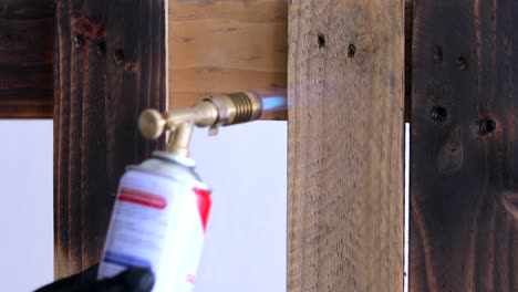 person with handheld butane blowtorch blackening the surface of pallet