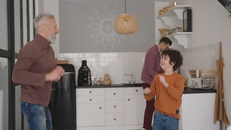 un hombre gay le enseña a su hijo a bailar mientras su pareja prepara el desayuno.