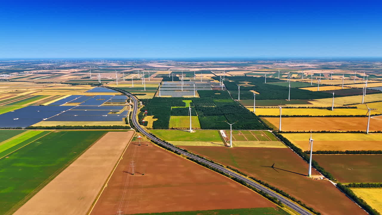 Modern highway crosses the rural area. Vast countryside with electricity power lines, solar panels and wind mills on sunny day. Aerial view